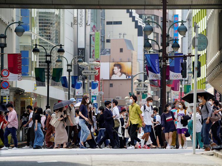 Pedestres usam máscaras de proteção enquanto caminham sob rua decorada para os Jogos Olímpicos e Paralímpicos da Tóquio-2020 no Japão - anéis - transeuntes - Olimpíada