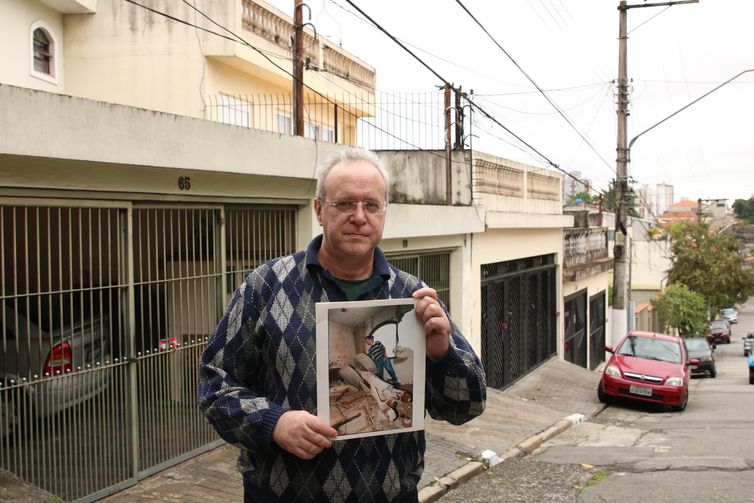 O jornalista Jorge Tadeu da Silva, um dos afetados pelo acidente com o avião modelo Fokker 100 da TAM que vitmou 99 pessoas em 1996, segura foto de como ficou a casa dele na rua Luís Orsini de Castro, no Jabaquara.