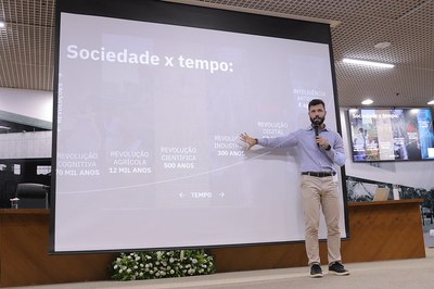 Neurocientista Daniel Hosken audiodescrição: Neurocientista Daniel Hosken em frente ao telão retroprojetor
