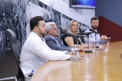 Dr. Tomaz de Aquino audiodescrição: Dr. Tomaz de Aquino fala na mesa de abertura ao lado das demais autoridades.
