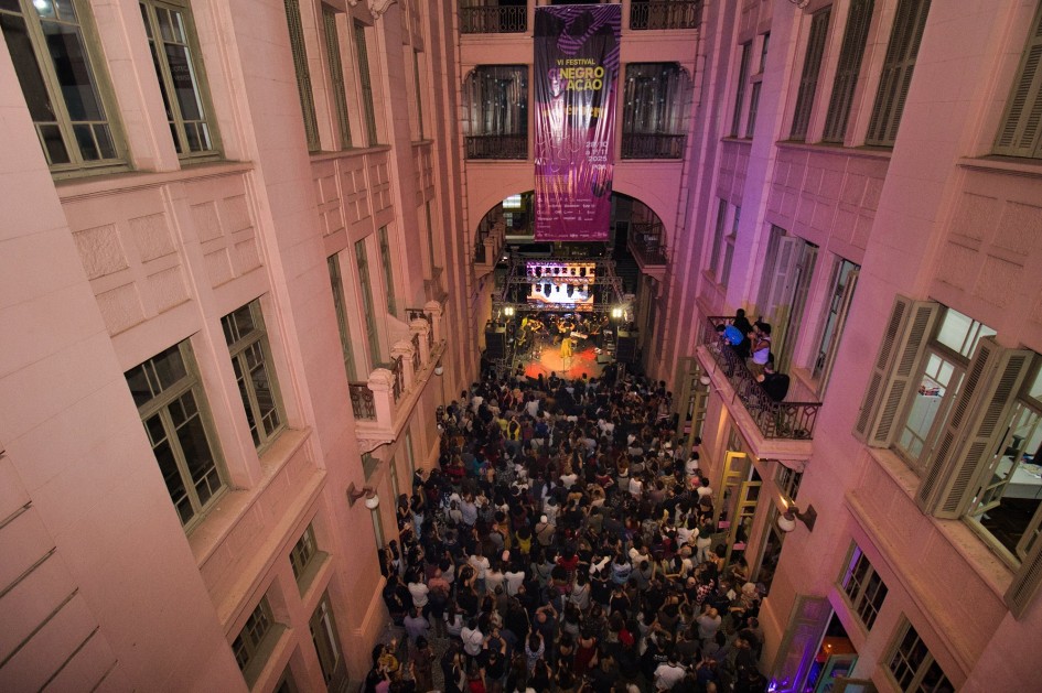 Imagem mostra de cima o saguão da Casa de Cultura Mario Quintana, lotada de pessoas que acompanham a premiação e show no palco, ao fundo.